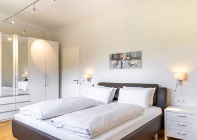Hotelzimmer mit Doppelbett, heller Wandfarbe und Nachttischlampen.