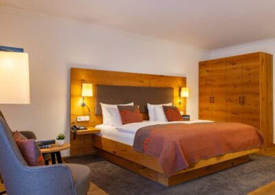 Hotelzimmer mit Doppelbett, orangener Tagesdecke, zwei Nachttischen mit Lampen und grauem Teppichboden.