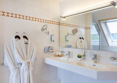 Großes Badezimmer mit zwei Waschbecken, Spiegeln und Bademänteln.