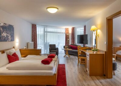 Helles Hotelzimmer mit Doppelbett, Sofa und Tisch, Zugang zum Balkon.