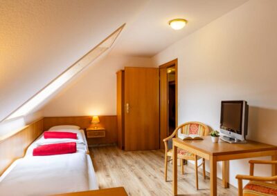 Dachzimmer mit zwei Einzelbetten, Holzschrank und kleiner Sitzecke.