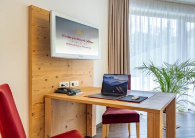 Arbeitsbereich im Hotelzimmer mit Holzschreibtisch, Stuhl und TV an der Wand.