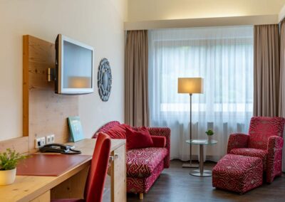 Hotelzimmer mit zwei roten Sesseln, Beistelltisch und Stehlampe.